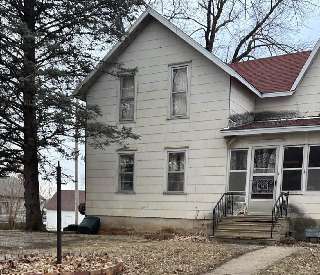 The same house in colour in 2022, with white siding, a red roof and a screened front porch