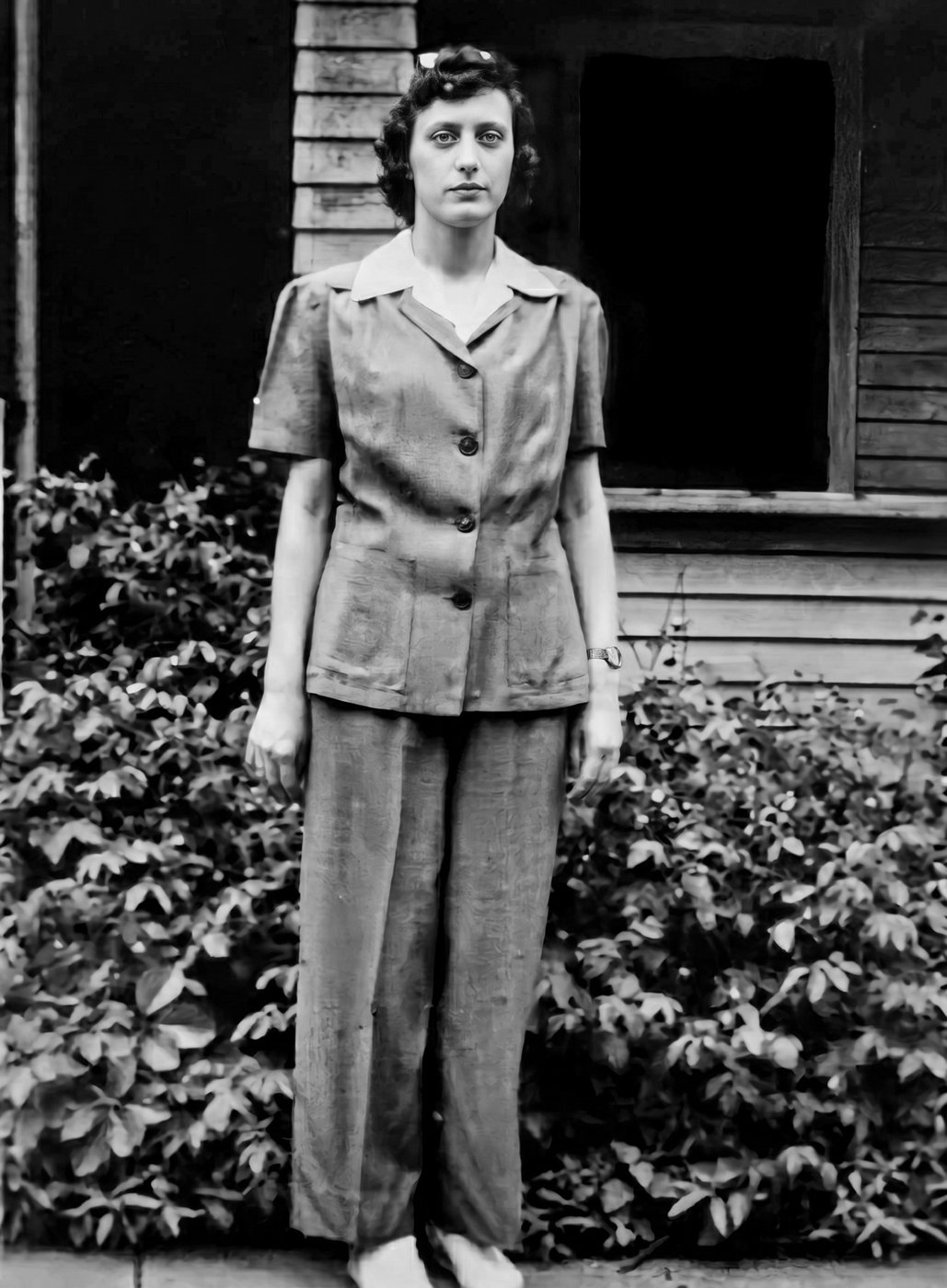 Norma standing in front of a house wearing a work shirt and trousers